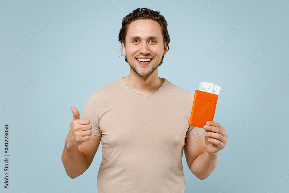 Traveler tourist man in casual basic t-shirt hold passport tickets show thumb up gesture isolated on pastel blue background. Passenger traveling abroad weekends getaway Air flight journey concept Traveler tourist man in casual basic t-shirt hold passport tickets show thumb up gesture isolated on pastel blue background. Passenger traveling abroad weekends getaway Air flight journey concept