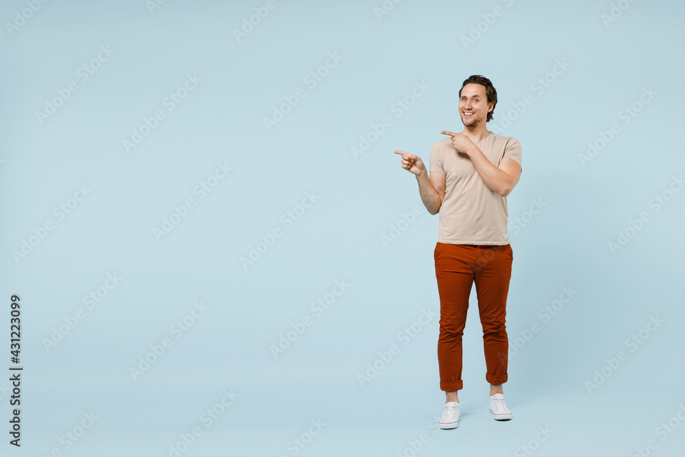 Full length young smiling happy positive caucasian man 20s wear casual basic beige t-shirt point index finger aside on copy space area mock up isolated on pastel blue color background studio portrait Full length young smiling happy positive caucasian man 20s wear casual basic beige t-shirt point index finger aside on copy space area mock up isolated on pastel blue color background studio portrait