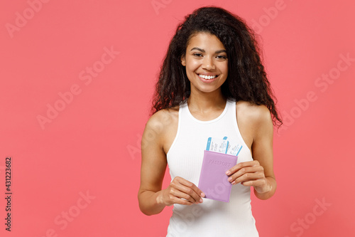 Traveler tourist smiling happy african american woman in white tank shirt hold passport tickets isolated on pink background. Passenger traveling abroad on weekends getaway. Air flight journey concept.
