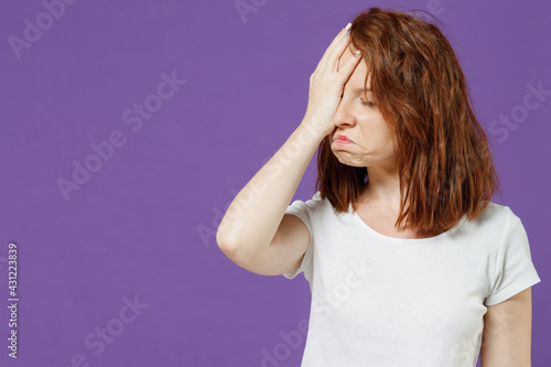 Young sad mistaken confused astonished disappointed caucasian woman 20s wear white basic t-shirt put hand on face facepalm epic fail gesture isolated on dark violet color background studio portrait photo