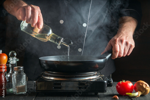 The chef or cook adds olive oil to the pan while cooking. Working environment on the restaurant kitchen table