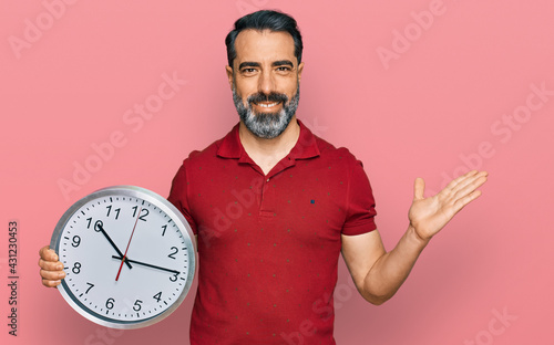 Middle aged man with beard holding big clock celebrating victory with happy smile and winner expression with raised hands © Krakenimages.com