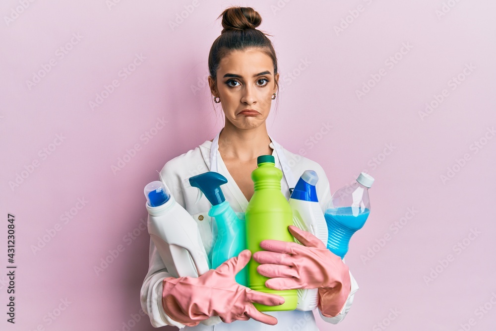 Beautiful brunette young woman wearing cleaner apron holding cleaning products depressed and worry for distress, crying angry and afraid. sad expression. Beautiful brunette young woman wearing cleaner apron holding cleaning products depressed and worry for distress, crying angry and afraid. sad expression.