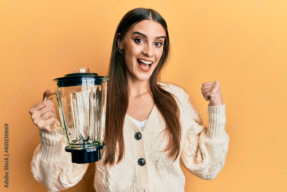 Beautiful brunette young woman holding food processor mixer machine pointing thumb up to the side smiling happy with open mouth Beautiful brunette young woman holding food processor mixer machine pointing thumb up to the side smiling happy with open mouth