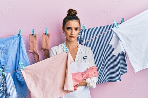 Beautiful brunette young woman washing clothes at clothesline skeptic and nervous, disapproving expression on face with crossed arms. negative person.