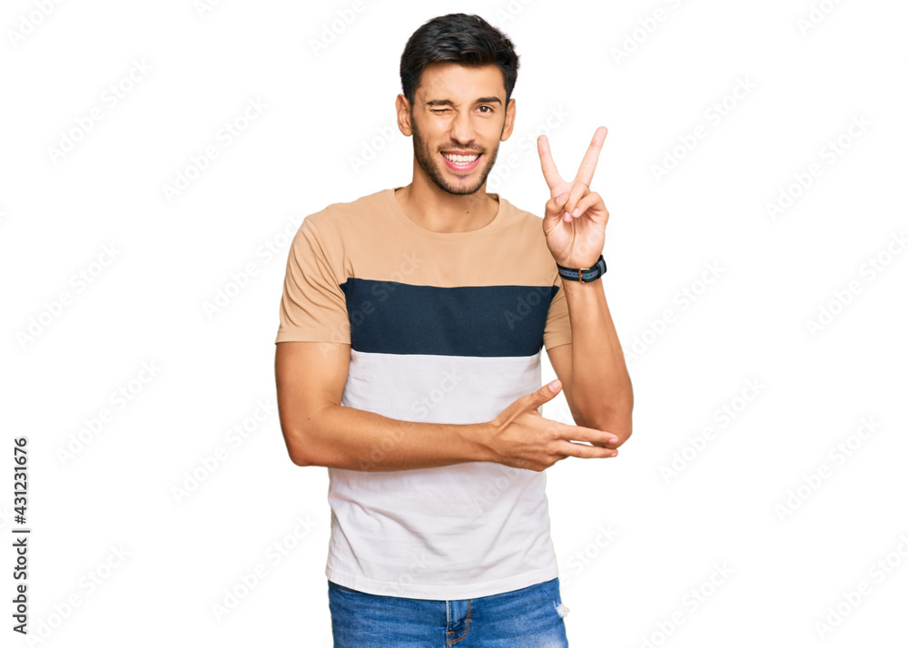 Young handsome man wearing casual clothes smiling with happy face winking at the camera doing victory sign with fingers. number two. Young handsome man wearing casual clothes smiling with happy face winking at the camera doing victory sign with fingers. number two.