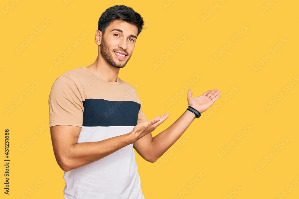 Young handsome man wearing casual clothes inviting to enter smiling natural with open hand Young handsome man wearing casual clothes inviting to enter smiling natural with open hand