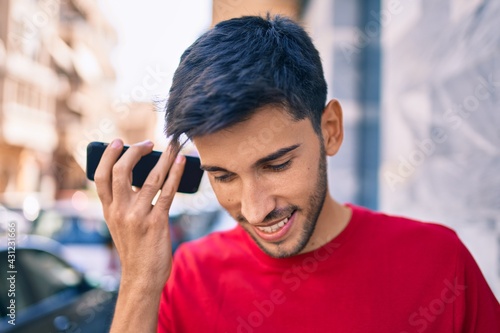 Young latin man smiling happy listening audio message using smartphone at the city.