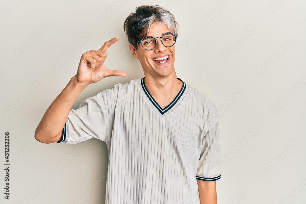 Young hispanic man wearing casual clothes and glasses smiling and confident gesturing with hand doing small size sign with fingers looking and the camera. measure concept. Young hispanic man wearing casual clothes and glasses smiling and confident gesturing with hand doing small size sign with fingers looking and the camera. measure concept.