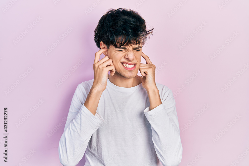 Handsome hipster young man wearing casual white shirt covering ears with fingers with annoyed expression for the noise of loud music. deaf concept. Handsome hipster young man wearing casual white shirt covering ears with fingers with annoyed expression for the noise of loud music. deaf concept.