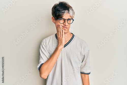 Young hispanic man wearing casual clothes and glasses touching mouth with hand with painful expression because of toothache or dental illness on teeth. dentist