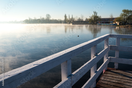 Jetty on a lake with fog. Wooden structure on the water. Sunrise and fog over the water. © PhotoRK