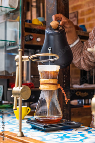 Professional barista preparing coffee using chemex pour over coffee maker and drip kettle. Alternative ways of brewing coffee. Coffee shop concept. Yellow cups