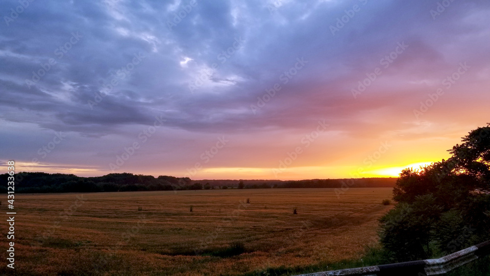 beautiful violet-orange sunset over a mown wheat field, the sky is covered with clouds