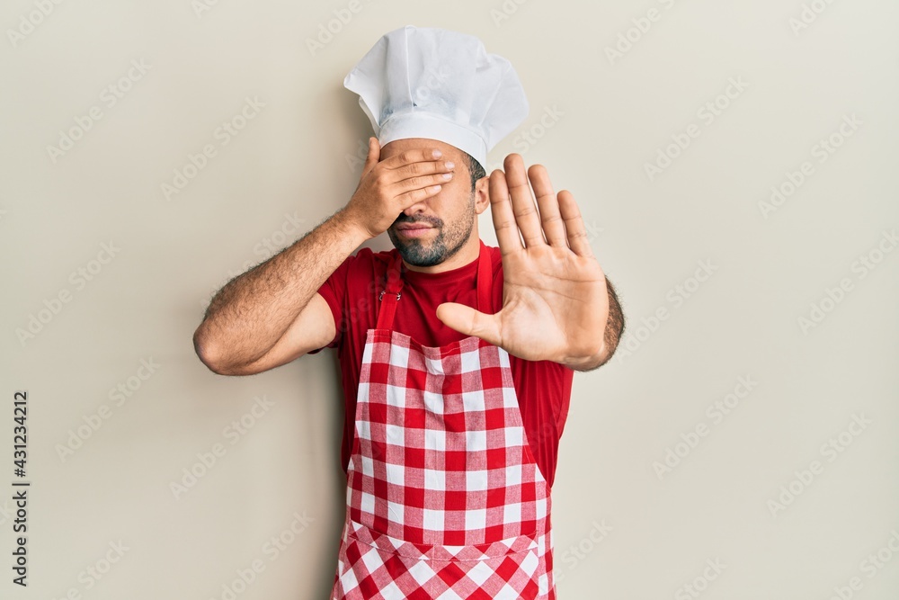 Young hispanic man wearing baker uniform covering eyes with hands and doing stop gesture with sad and fear expression. embarrassed and negative concept. Young hispanic man wearing baker uniform covering eyes with hands and doing stop gesture with sad and fear expression. embarrassed and negative concept.