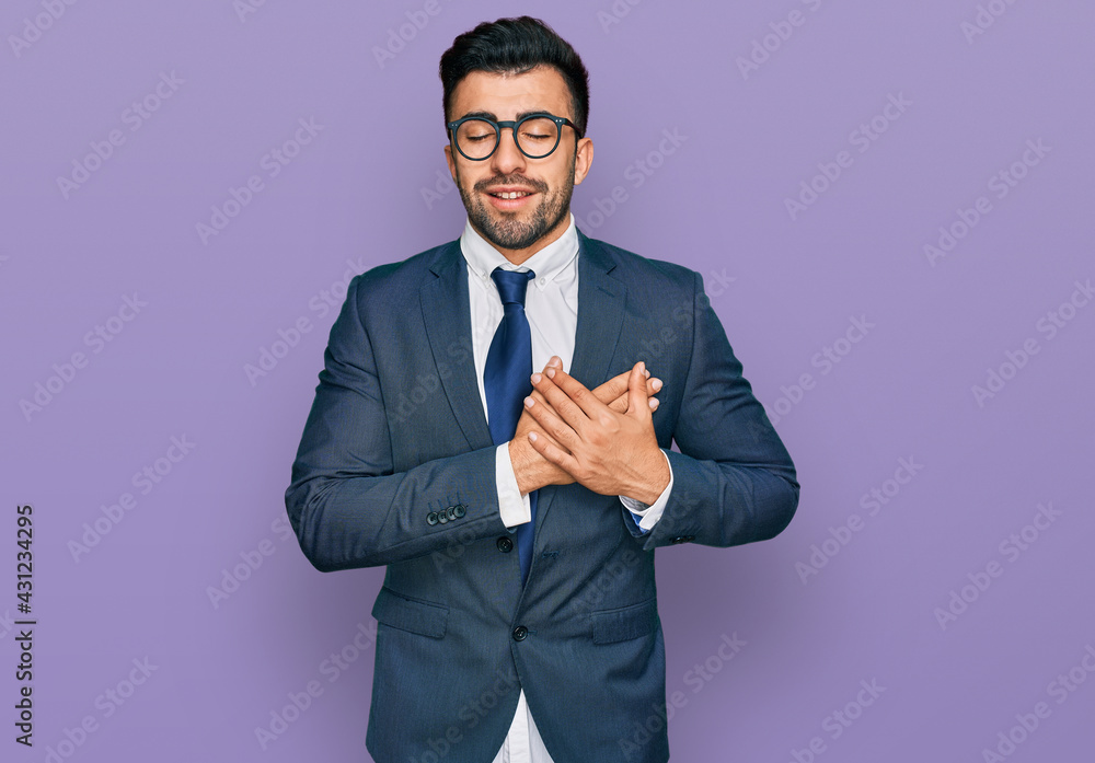 Hispanic man with beard wearing business suit and tie smiling with hands on chest with closed eyes and grateful gesture on face. health concept. Hispanic man with beard wearing business suit and tie smiling with hands on chest with closed eyes and grateful gesture on face. health concept.