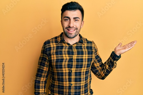 Young hispanic man wearing casual clothes smiling cheerful presenting and pointing with palm of hand looking at the camera.