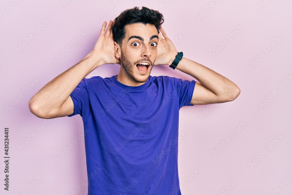 Young hispanic man wearing casual t shirt smiling cheerful playing peek a boo with hands showing face. surprised and exited Young hispanic man wearing casual t shirt smiling cheerful playing peek a boo with hands showing face. surprised and exited