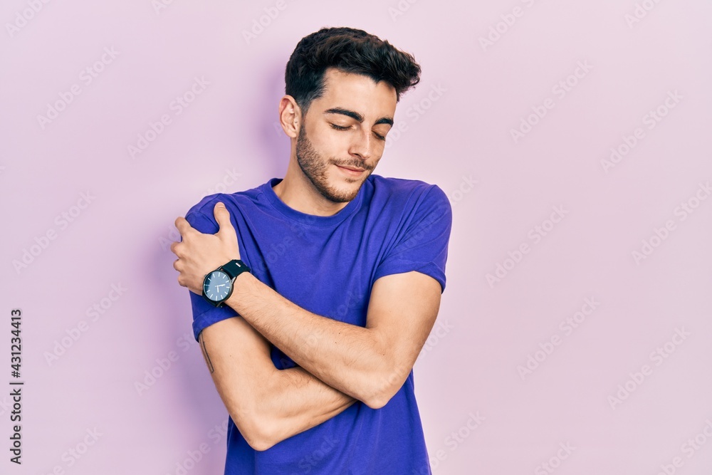Young hispanic man wearing casual t shirt hugging oneself happy and positive, smiling confident. self love and self care Young hispanic man wearing casual t shirt hugging oneself happy and positive, smiling confident. self love and self care