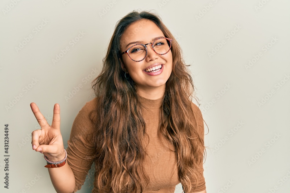 Young hispanic girl wearing casual clothes and glasses smiling looking to the camera showing fingers doing victory sign. number two. Young hispanic girl wearing casual clothes and glasses smiling looking to the camera showing fingers doing victory sign. number two.