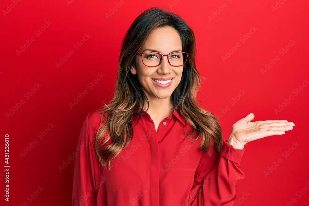 Young latin woman wearing casual clothes and glasses smiling cheerful presenting and pointing with palm of hand looking at the camera. Young latin woman wearing casual clothes and glasses smiling cheerful presenting and pointing with palm of hand looking at the camera.