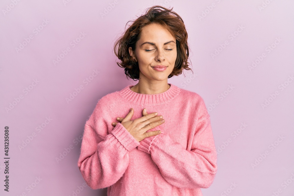 Young brunette woman wearing casual winter sweater smiling with hands on chest, eyes closed with grateful gesture on face. health concept.