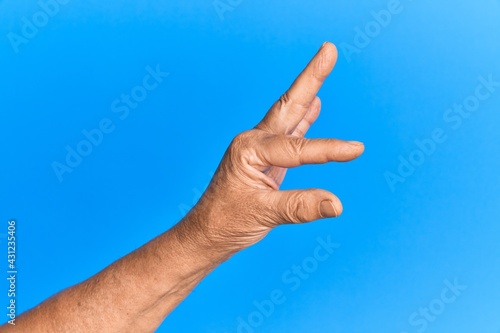Hand of senior hispanic man over blue isolated background picking and taking invisible thing, holding object with fingers showing space © Krakenimages.com