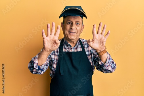 Handsome senior man with grey hair wearing welding protection mask showing and pointing up with fingers number nine while smiling confident and happy.