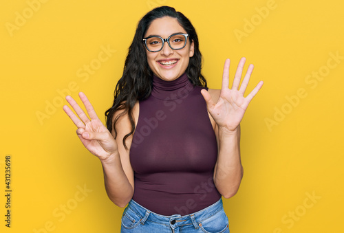 Brunette young woman wearing casual clothes and glasses showing and pointing up with fingers number eight while smiling confident and happy.