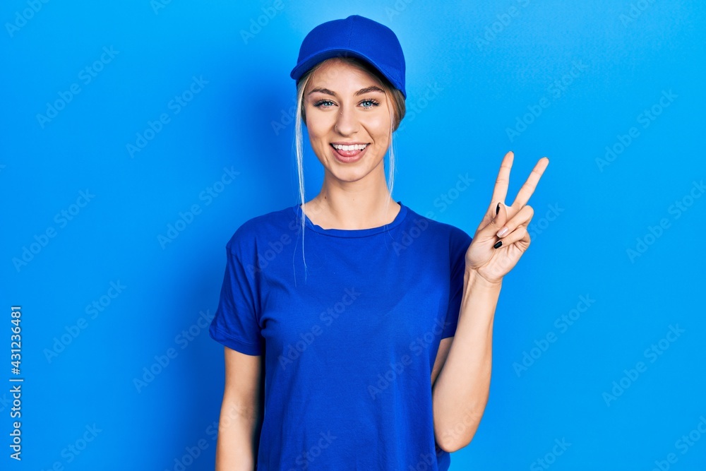 Young caucasian woman wearing courier uniform wearing cap smiling with happy face winking at the camera doing victory sign. number two. Young caucasian woman wearing courier uniform wearing cap smiling with happy face winking at the camera doing victory sign. number two.