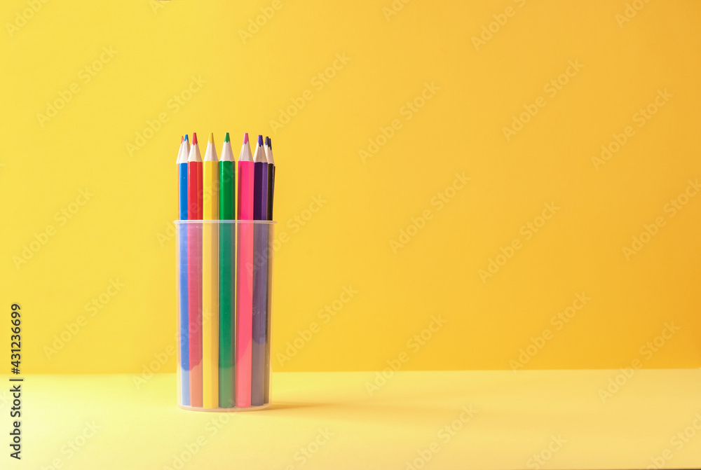 Colored pencils in a plastic cup on a yellow-orange background. Colored pencils in a plastic cup on a yellow-orange background.