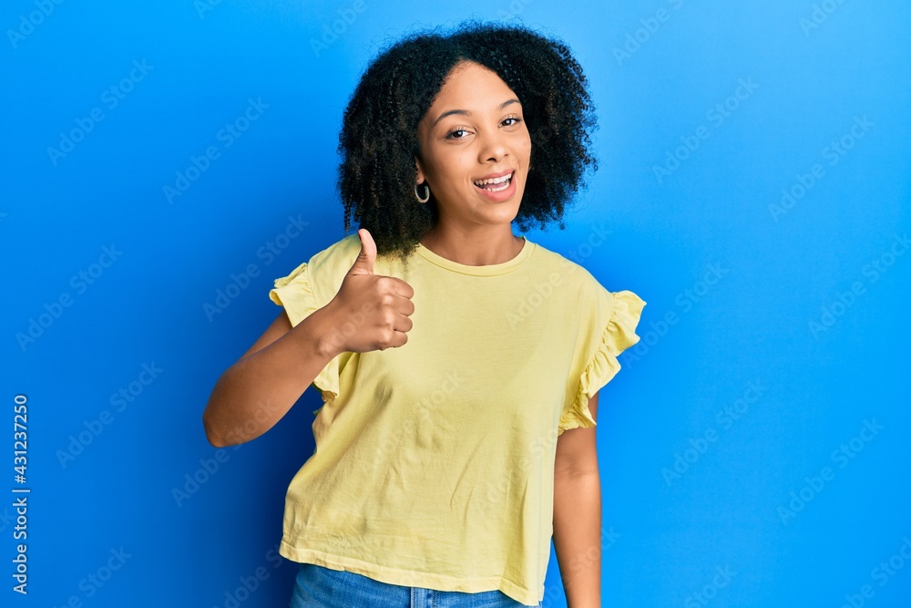 Young african american girl wearing casual clothes doing happy thumbs up gesture with hand. approving expression looking at the camera showing success. Young african american girl wearing casual clothes doing happy thumbs up gesture with hand. approving expression looking at the camera showing success.