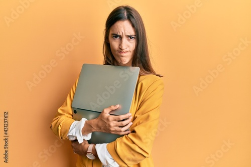 Young beautiful woman holding laptop skeptic and nervous, frowning upset because of problem. negative person.