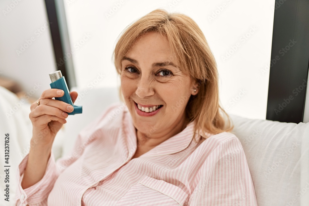 Middle age asthmatic woman smiling happy using inhaler lying on the bed at home. Middle age asthmatic woman smiling happy using inhaler lying on the bed at home.