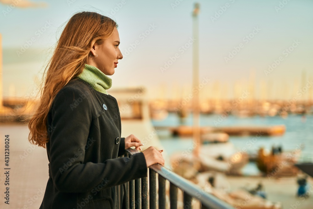 Young blonde girl smiling happy leaning on the balustrade at the city. Young blonde girl smiling happy leaning on the balustrade at the city.