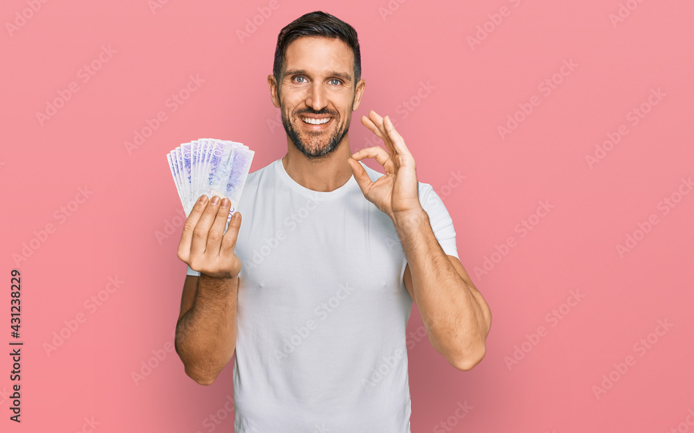 Handsome man with beard holding 20 swedish krona banknotes doing ok sign with fingers, smiling friendly gesturing excellent symbol Handsome man with beard holding 20 swedish krona banknotes doing ok sign with fingers, smiling friendly gesturing excellent symbol