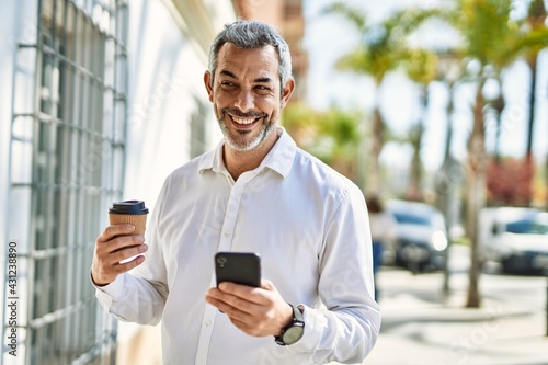 Middle age grey-haired man using smartphone drinking coffee at the city.