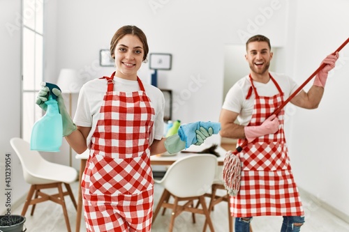 Bild auf Leinwand Young caucasian couple cleaning using mop as a guitar at home.