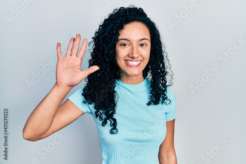 Young hispanic woman with curly hair wearing casual blue t shirt showing and pointing up with fingers number five while smiling confident and happy.