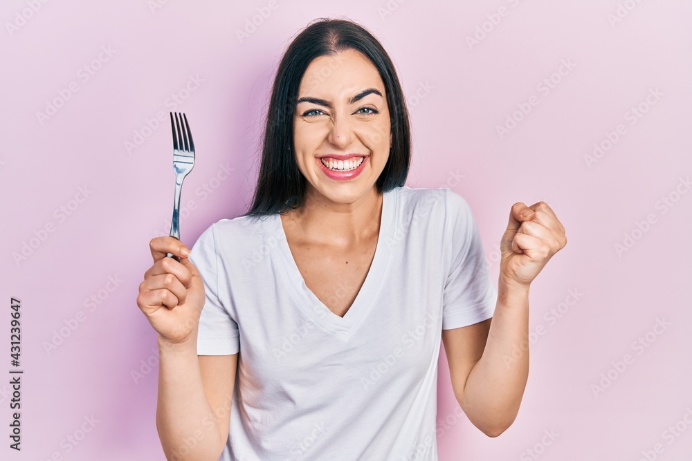 Beautiful woman with blue eyes holding one silver fork screaming proud, celebrating victory and success very excited with raised arm Beautiful woman with blue eyes holding one silver fork screaming proud, celebrating victory and success very excited with raised arm