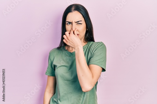 Foto Beautiful woman with blue eyes wearing casual t shirt smelling something stinky and disgusting, intolerable smell, holding breath with fingers on nose