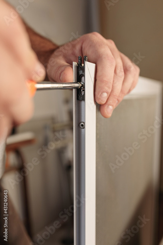 Man hand with screwdriver tool to assemble an aluminum window screen. Selective focus. Vertical image.