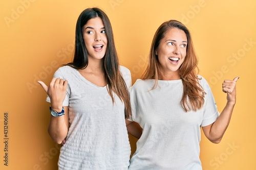 Hispanic family of mother and daughter wearing casual white tshirt smiling with happy face looking and pointing to the side with thumb up.