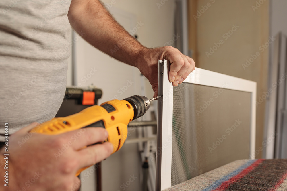 Man's hand with a drill to assemble an aluminum window screen. Selective focus. Horizontal image. Man's hand with a drill to assemble an aluminum window screen. Selective focus. Horizontal image.
