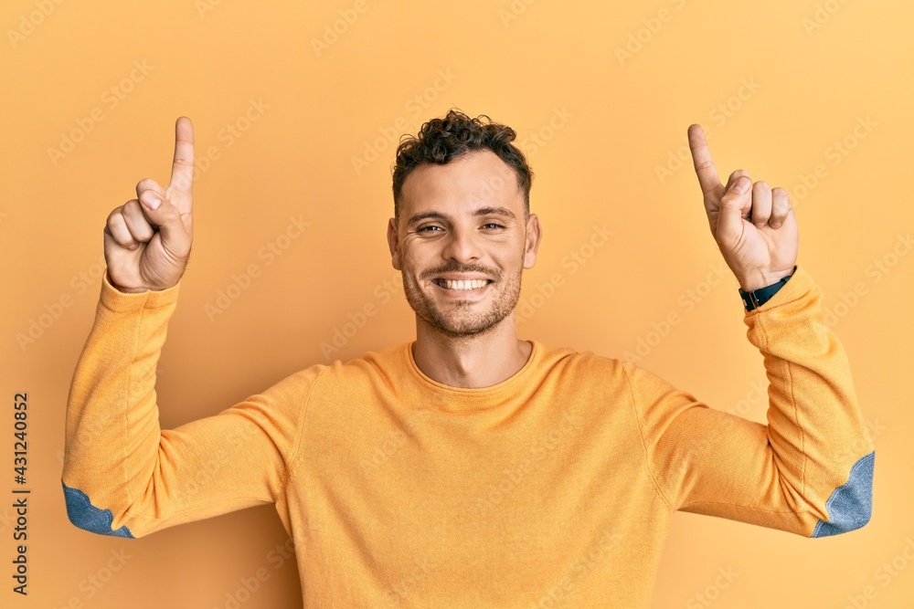 Young hispanic man pointing up with fingers smiling with a happy and cool smile on face. showing teeth. Young hispanic man pointing up with fingers smiling with a happy and cool smile on face. showing teeth.