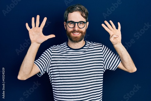 Caucasian man with beard wearing striped t shirt and glasses showing and pointing up with fingers number nine while smiling confident and happy.