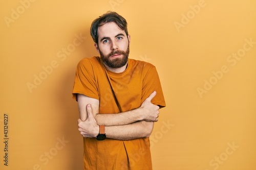 Caucasian man with beard wearing casual yellow t shirt shaking and freezing for winter cold with sad and shock expression on face