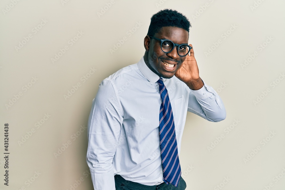 Handsome black man wearing glasses business shirt and tie smiling with hand over ear listening an hearing to rumor or gossip. deafness concept.