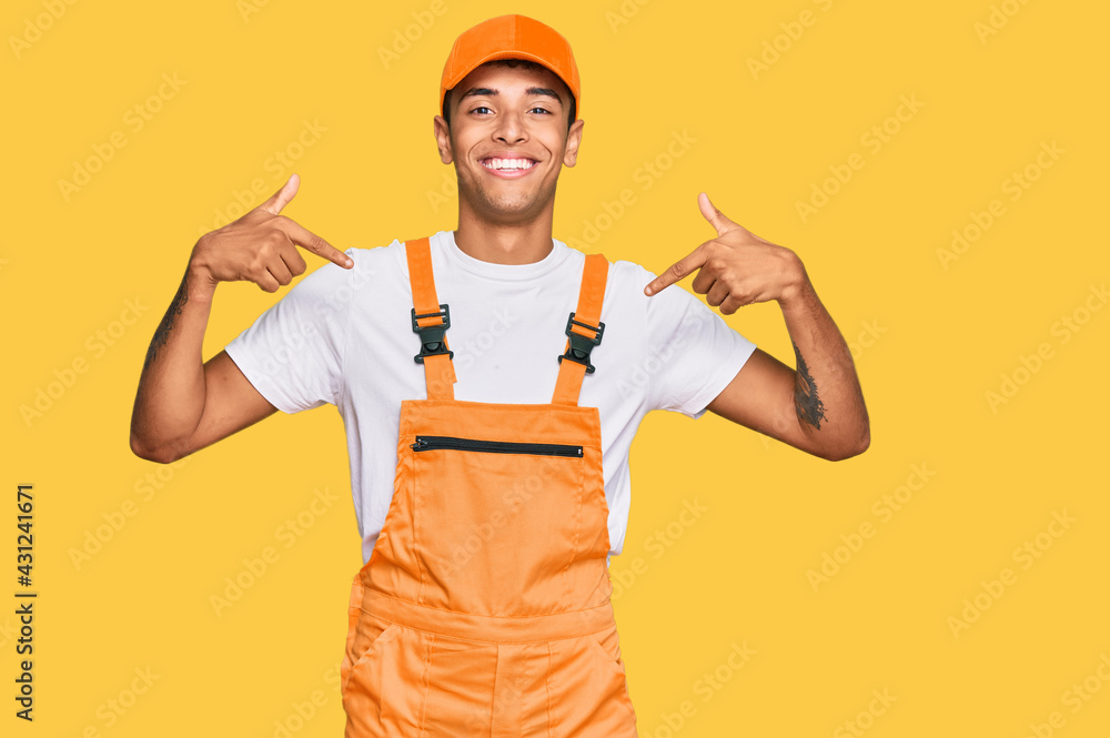 Young handsome african american man wearing handyman uniform looking confident with smile on face, pointing oneself with fingers proud and happy. Young handsome african american man wearing handyman uniform looking confident with smile on face, pointing oneself with fingers proud and happy.