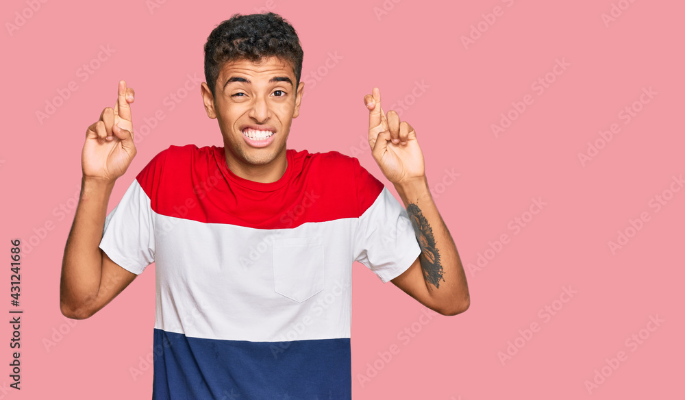 Young handsome african american man wearing casual clothes gesturing finger crossed smiling with hope and eyes closed. luck and superstitious concept. Young handsome african american man wearing casual clothes gesturing finger crossed smiling with hope and eyes closed. luck and superstitious concept.